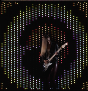 image of lady playing guitar in front of a light wall